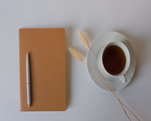 A notebook and pen on a clean desk beside a cup of tea
